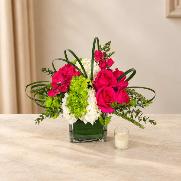 Pink roses and white hydrangeas in a square glass vase with a small candle nearby.