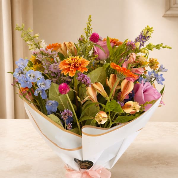 Mixed bouquet of colorful flowers wrapped in white paper with a pink ribbon