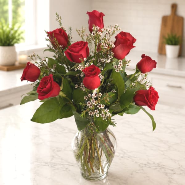Red roses arranged in a clear glass vase with small white filler flowers