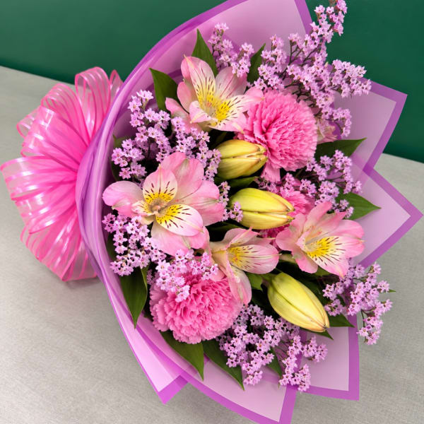 Pink bouquet with lilies, carnations, and purple filler flowers wrapped in purple paper
