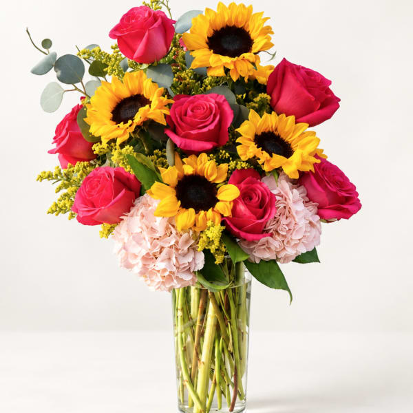 Bouquet of pink roses, sunflowers, and pale hydrangeas in a clear glass vase