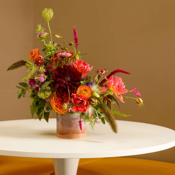 Colorful mixed flower arrangement in a low glass vase on a white table