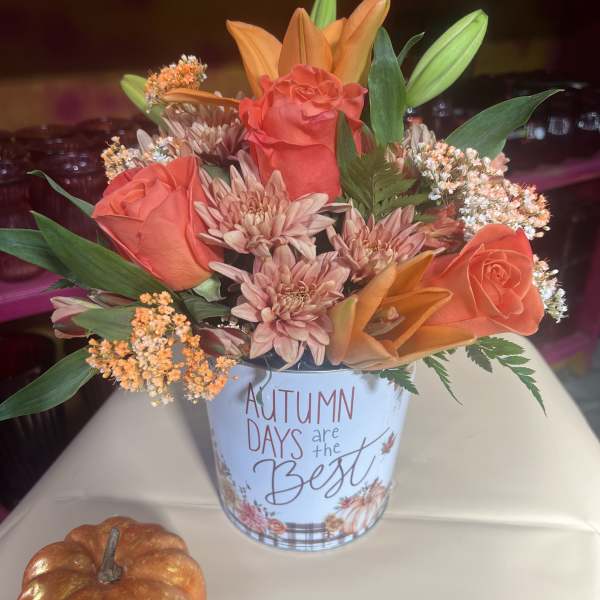 Autumn floral arrangement in a printed tin with orange roses and lilies