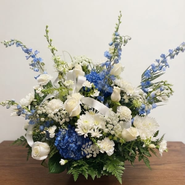 Blue and white floral arrangement with roses and ribbon in a low container