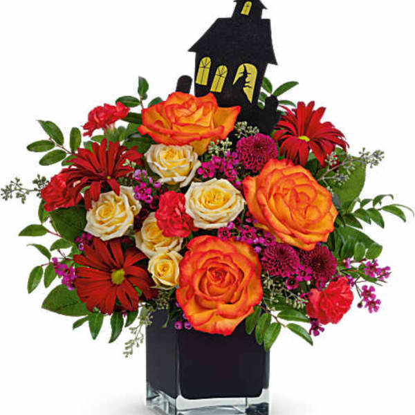 Bouquet of orange roses and red daisies in a black vase with a Halloween house pick