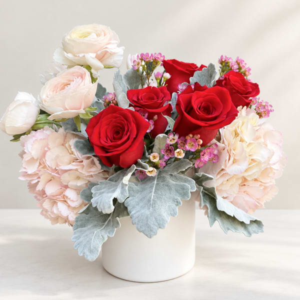Red roses and pale pink flowers arranged in a white vase