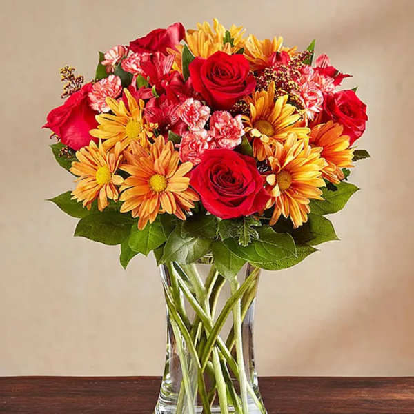 Bouquet of red roses and yellow daisies in a clear glass vase