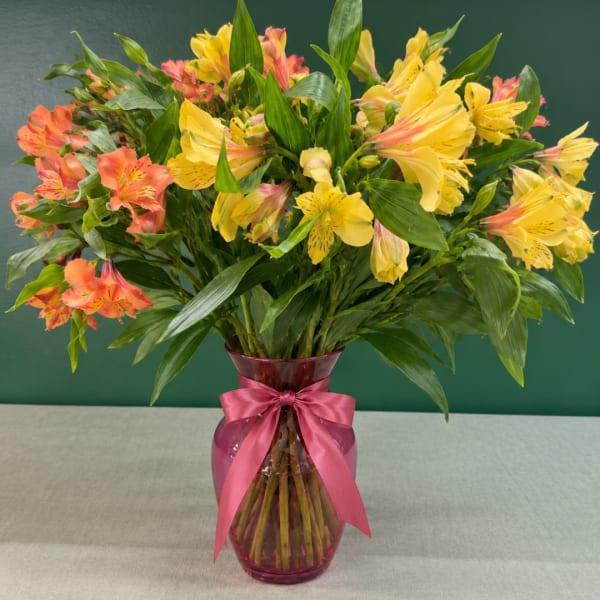Bouquet of yellow and coral alstroemeria in a pink glass vase with a ribbon