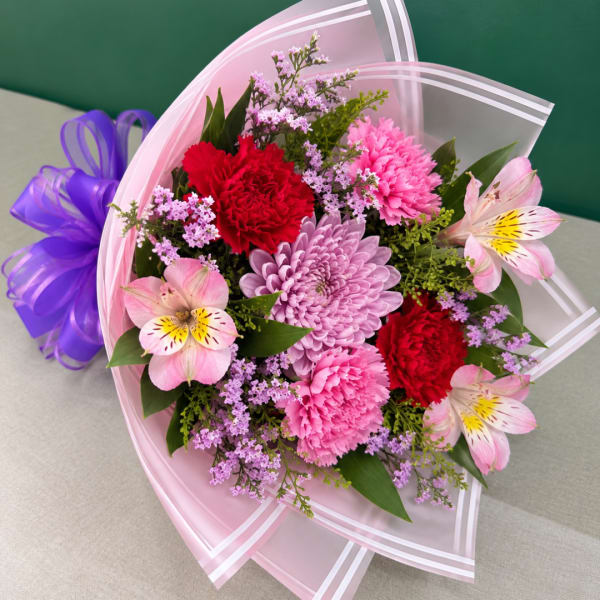 Bouquet of pink, red, and lavender flowers wrapped in pink paper with a purple ribbon