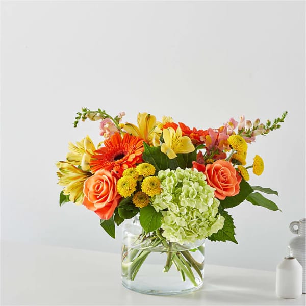 Colorful bouquet of roses, gerbera daisies, hydrangea, and mixed blooms in a glass vase