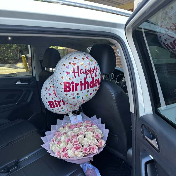 Pink and white rose bouquet with birthday balloons in a car seat