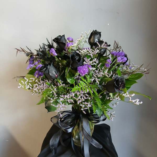 Black roses and purple filler flowers in a glass vase with a black ribbon
