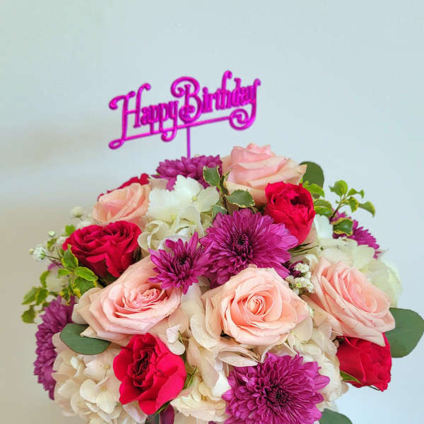 Pink and red flower arrangement in a mirrored vase with a Happy Birthday topper