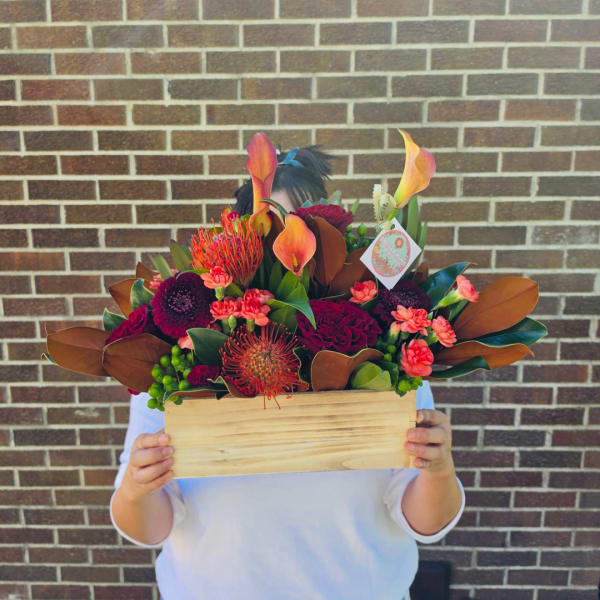 Mixed floral arrangement in a wooden box with orange calla lilies and deep red blooms
