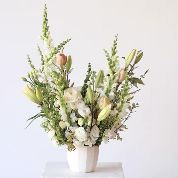 Tall white floral arrangement in a white vase with lilies, roses, and snapdragons