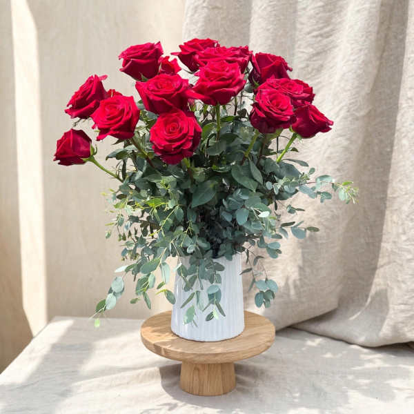 Red roses arranged in a white vase with trailing greenery