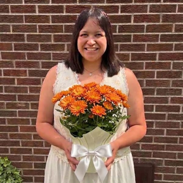 Woman holding a bouquet of orange daisies wrapped with a white ribbon