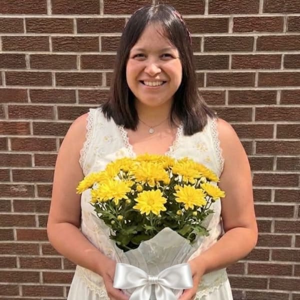 Woman holding a bouquet of yellow chrysanthemums wrapped in white paper with a bow
