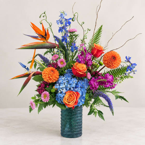 Colorful mixed bouquet in a textured blue vase with orange roses and blue hydrangea