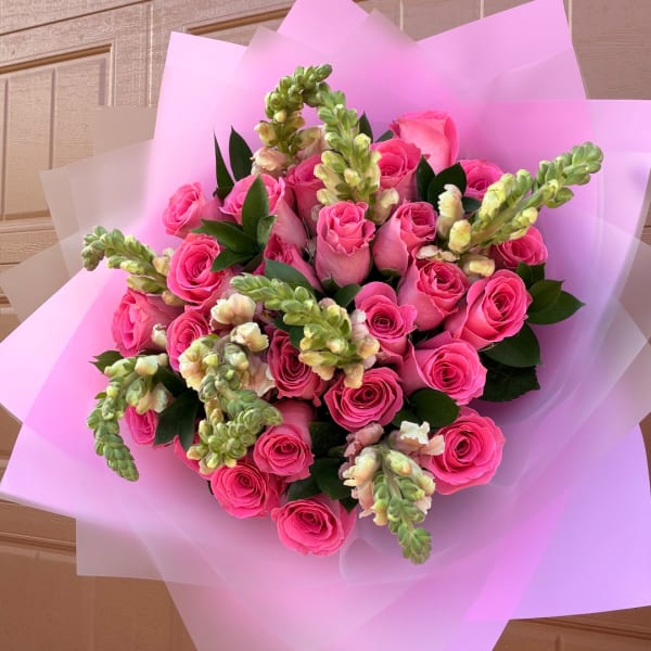 Bouquet of bright pink roses with green snapdragon spikes wrapped in pink paper