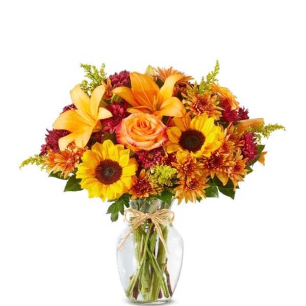 Bouquet of yellow lilies, sunflowers, and orange roses in a clear glass vase
