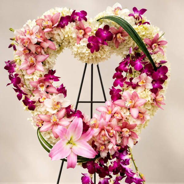 Heart-shaped floral wreath with pink and purple orchids on a stand