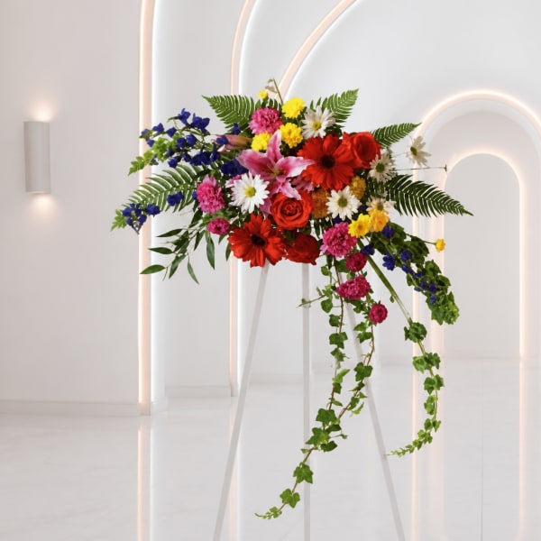 Colorful mixed flower arrangement on a white stand with trailing greenery