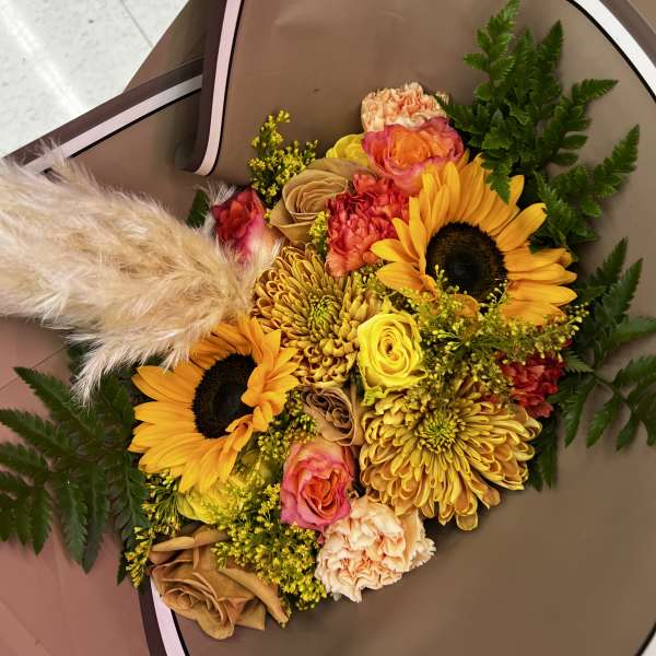 Bouquet of sunflowers, roses, and chrysanthemums wrapped in brown paper