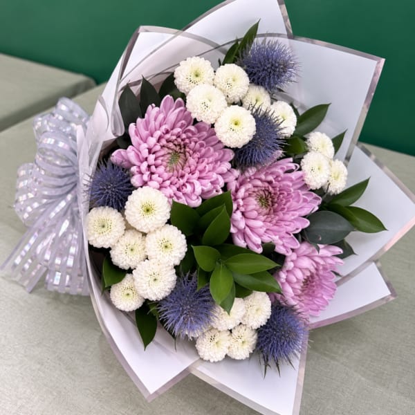Bouquet of pink chrysanthemums, white pompom flowers, and blue thistles wrapped in white paper