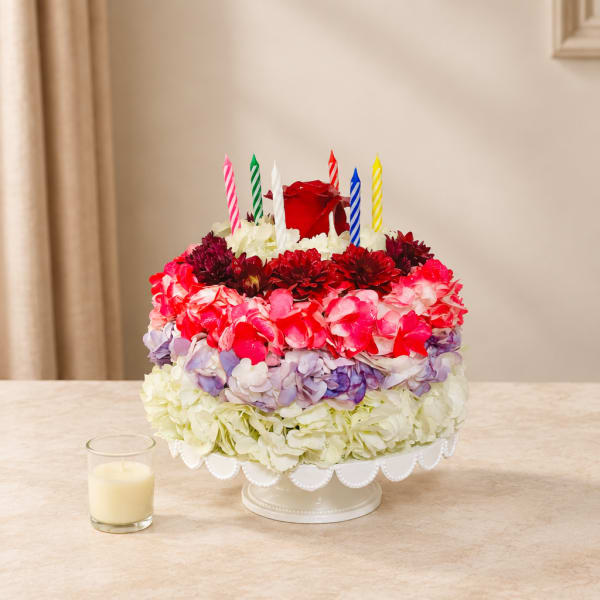 Round floral cake with colorful candles on a pedestal stand