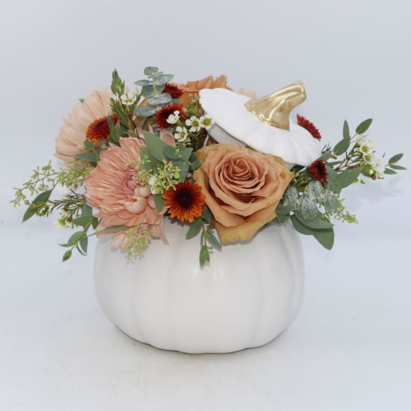 Floral arrangement in a white pumpkin container with peach and orange blooms