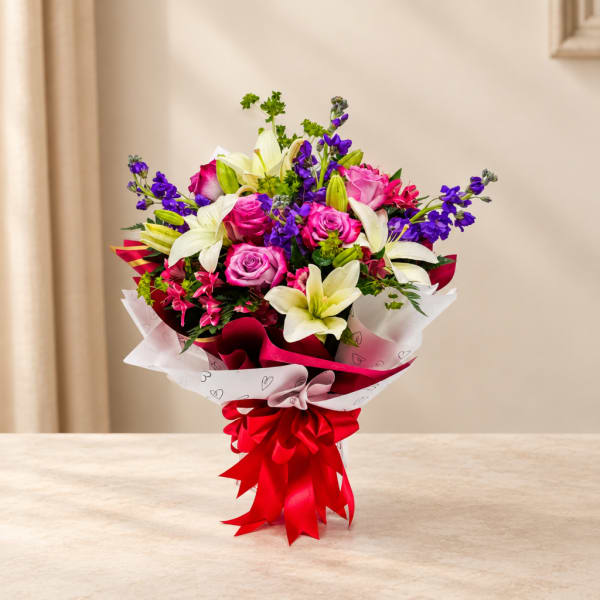 Bouquet of pink roses, white lilies, and purple flowers wrapped with red ribbon