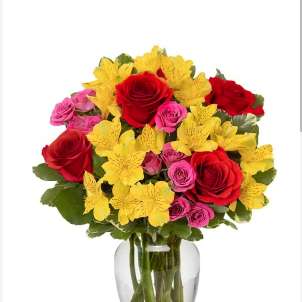 Bouquet of red roses, pink spray roses, and yellow flowers in a glass vase