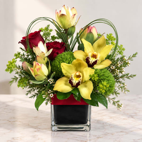 Arrangement of yellow orchids and red roses in a square glass vase