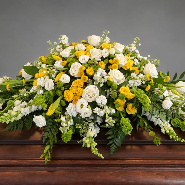 White and yellow floral casket spray on a wooden casket