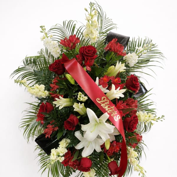 Standing funeral spray of red roses and white lilies with a red ribbon