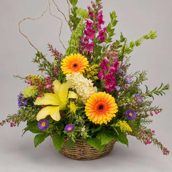 Basket arrangement with yellow lilies, orange gerberas, and purple flowers