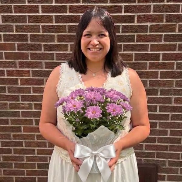 Woman holding a bouquet of purple daisies wrapped with a white ribbon
