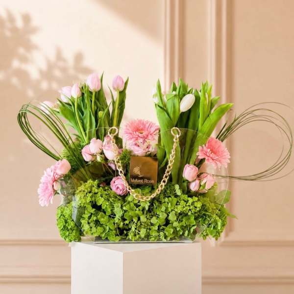 Pink tulips and roses arranged with pink daisies in a clear handbag-style container