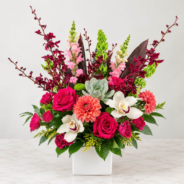 Bright mixed floral arrangement in a white square vase with roses and orchids
