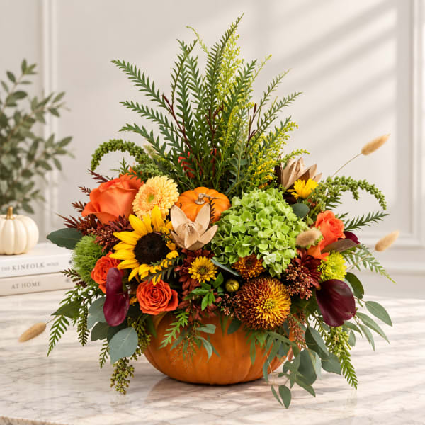 Autumn floral arrangement in a pumpkin container with orange, yellow, and green blooms