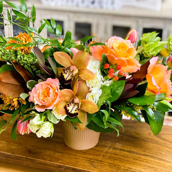 Mixed floral arrangement in a beige vase with peach roses and orchids