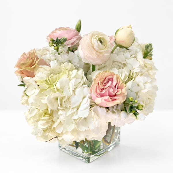 Pink and white flowers arranged in a clear square glass vase