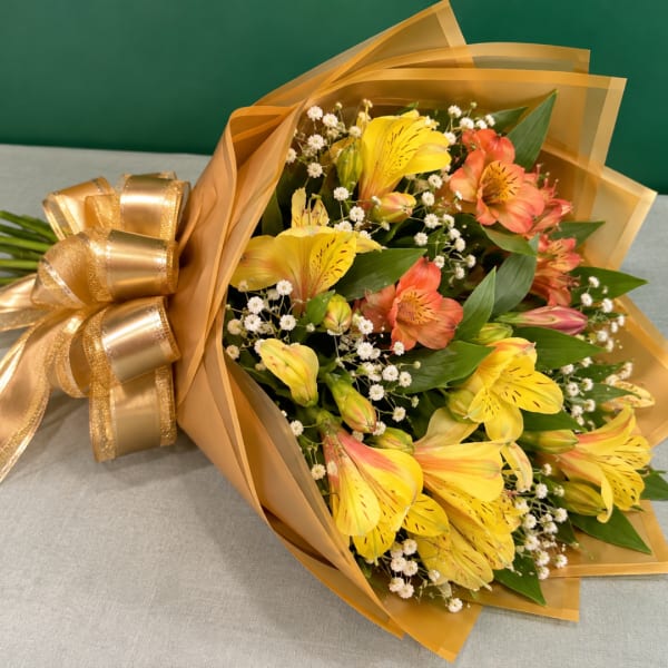 Bouquet of yellow and coral alstroemeria wrapped in gold paper with a ribbon