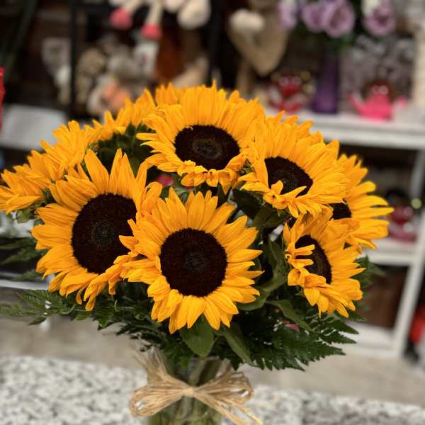 Bouquet of bright sunflowers in a clear glass vase with a raffia bow