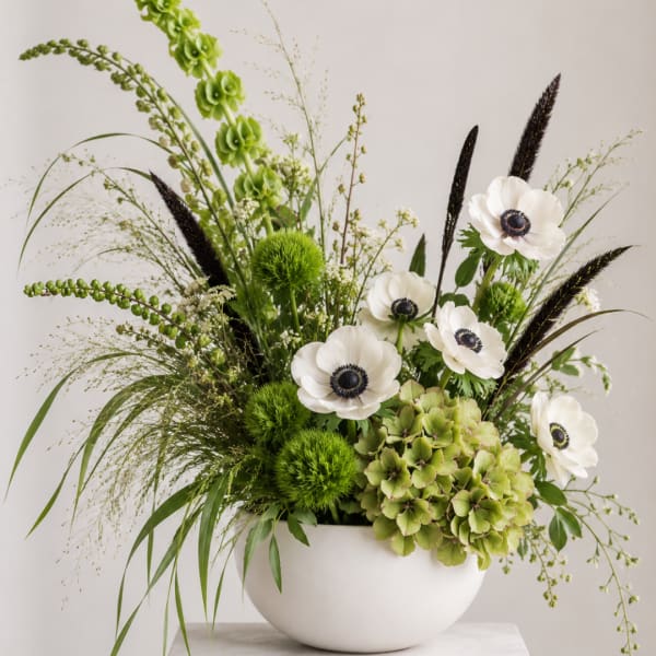 Green and white floral arrangement in a white bowl vase