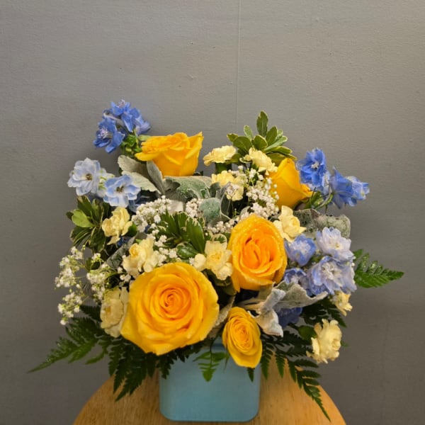 Yellow roses and blue flowers arranged in a light blue container
