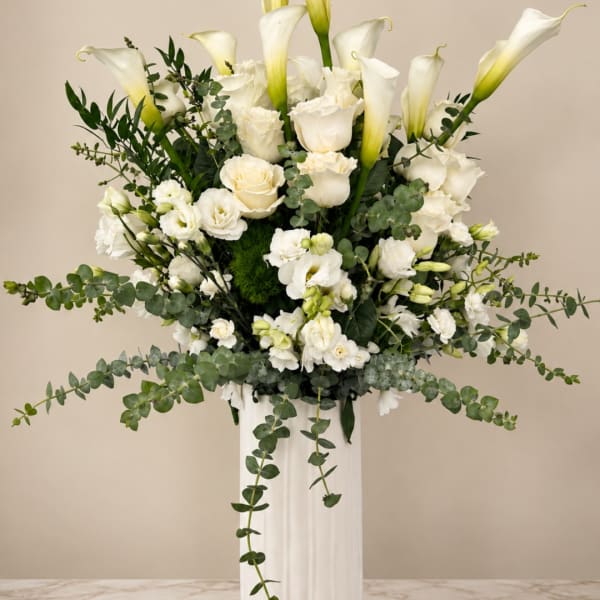 White calla lilies and roses in a tall white vase with trailing greenery