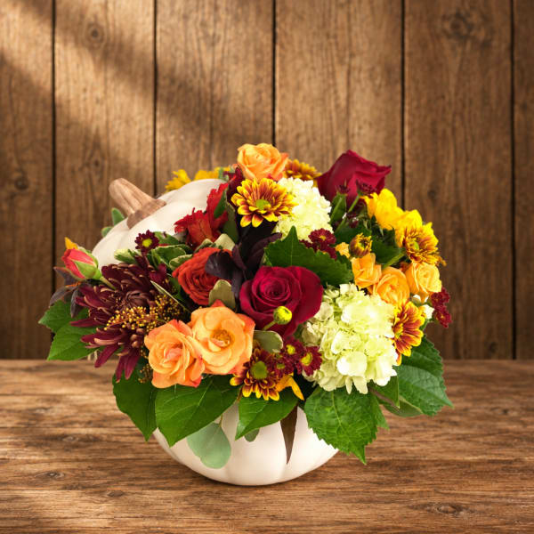 Mixed bouquet of roses, chrysanthemums, and hydrangeas in a white pumpkin vase