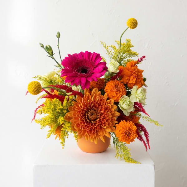 Orange and pink mixed flower arrangement in a round vase